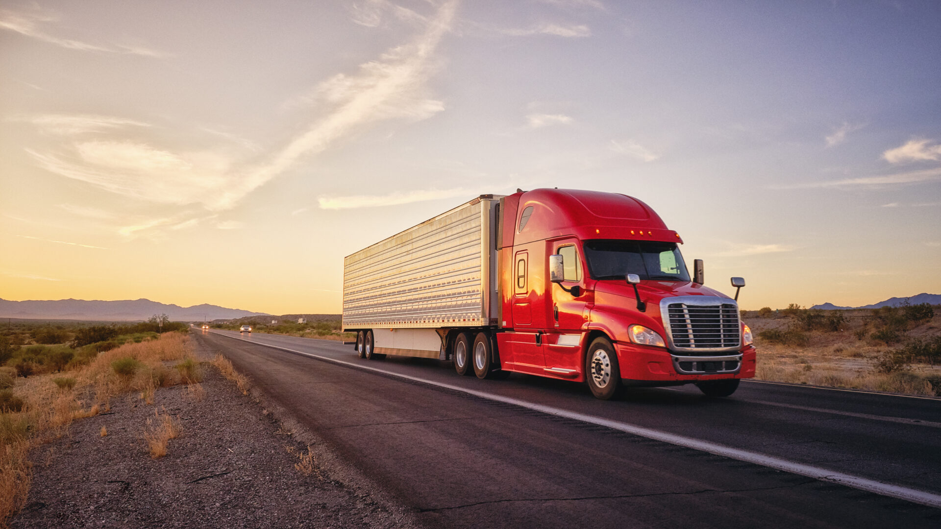 Large semi truck hauling freight on the open highway in the western USA under an evening sky.